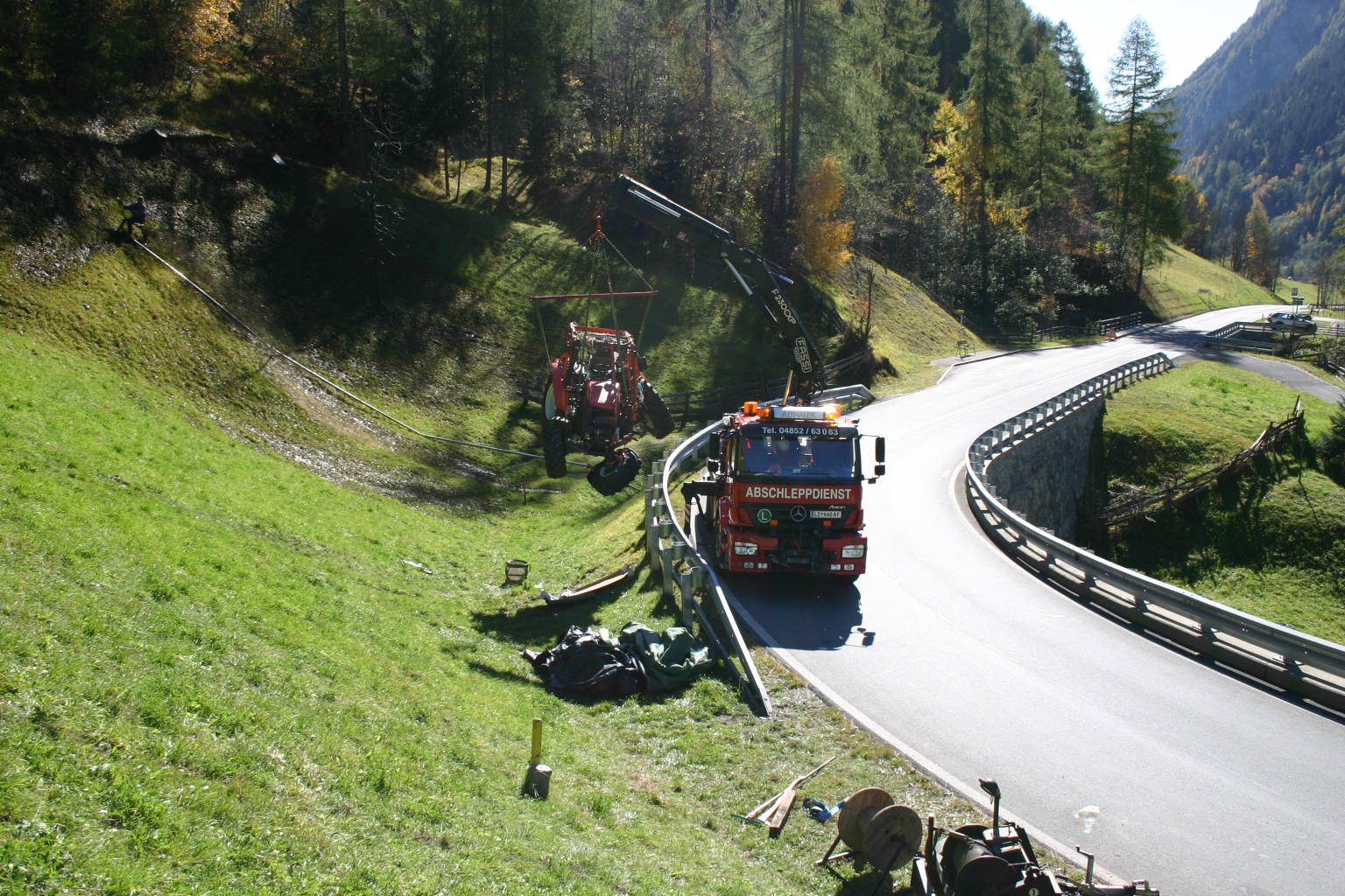 Ein Traktor wird von einem LKW mit Kran über die Leitplanke gehoben